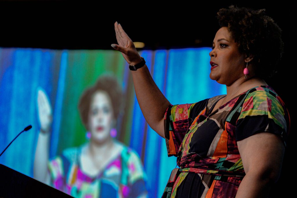 Color photo of Ijeoma Oluo speaking on the plenary stage at the 2023 NCWIT Summit.