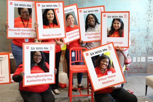 A group of women with frames embossed with Sit With Me branding held in front of them.